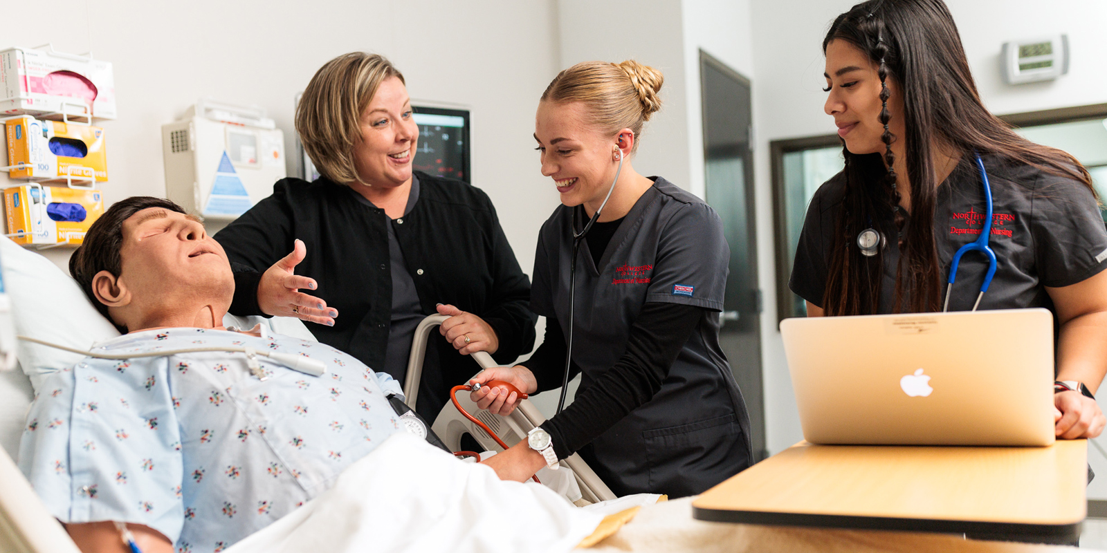 A nursing professor explains a treatment to two nursing students in a simulation lab