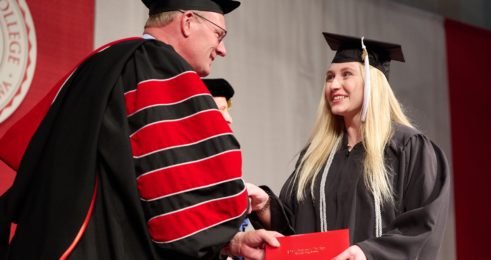 President Greg Christy hands a 2024 graduate her diploma